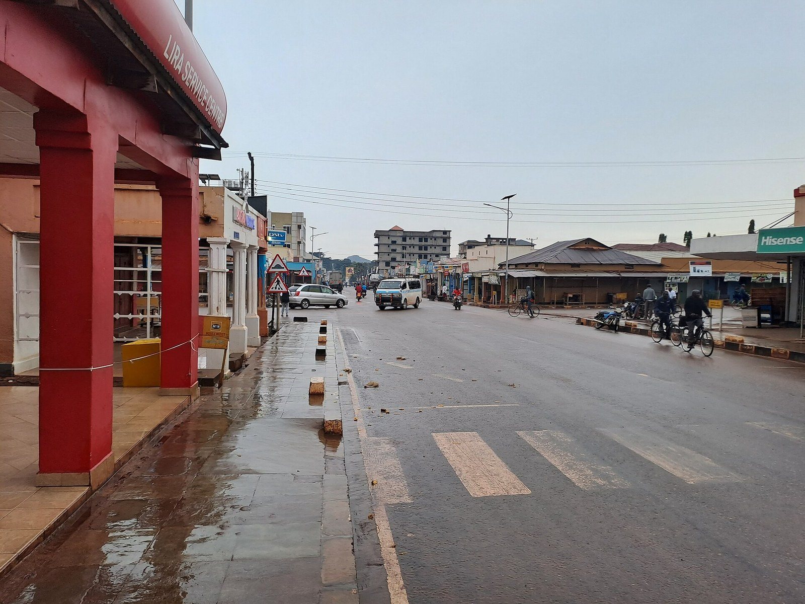 A wide Lira street just after rain — wet paving, a red-pillared shopfront on the left, a