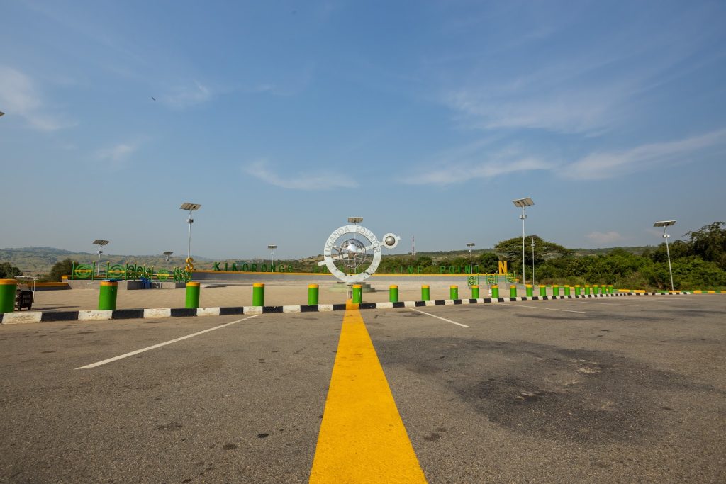 A wide tarmac road with painted lane markings running past the Kikorongo equator line point, open bush country beyond
