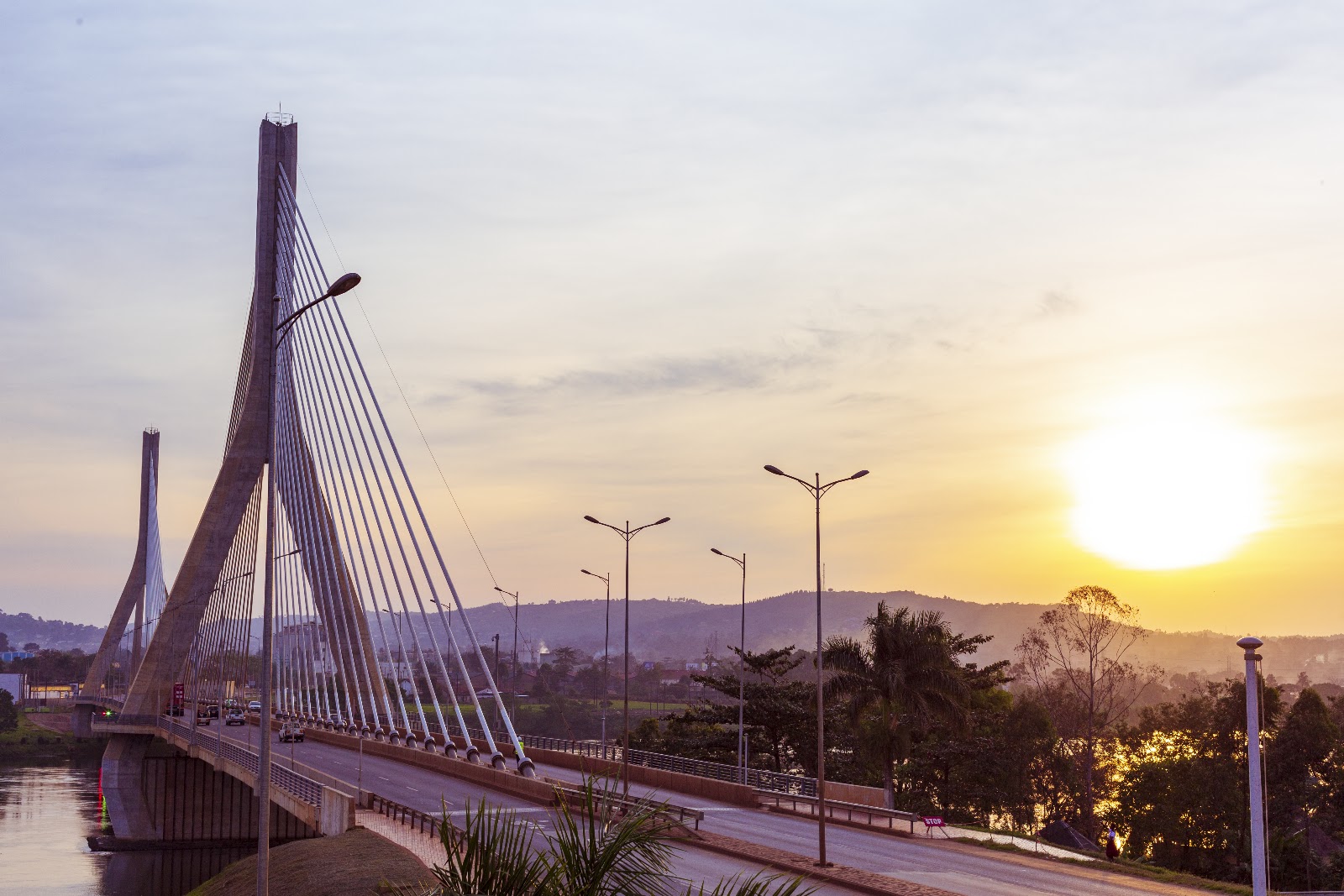 The cable-stayed Source of the Nile bridge at Jinja carrying its road deck across the river at sunset, with hills beyond
