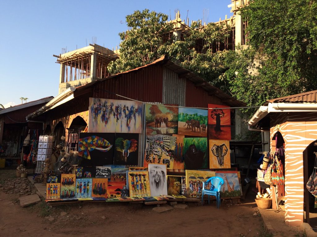 A roadside art stall hung with dozens of brightly painted canvases of wildlife and village scenes