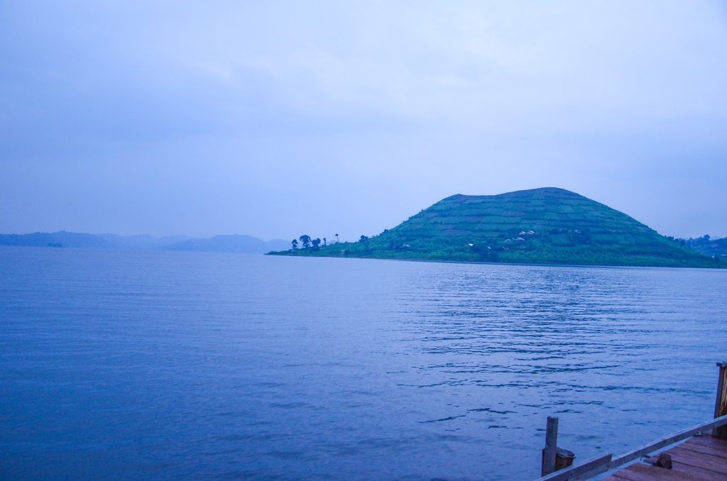 A steep green island rising from calm blue water under a hazy sky at Lake Bunyonyi