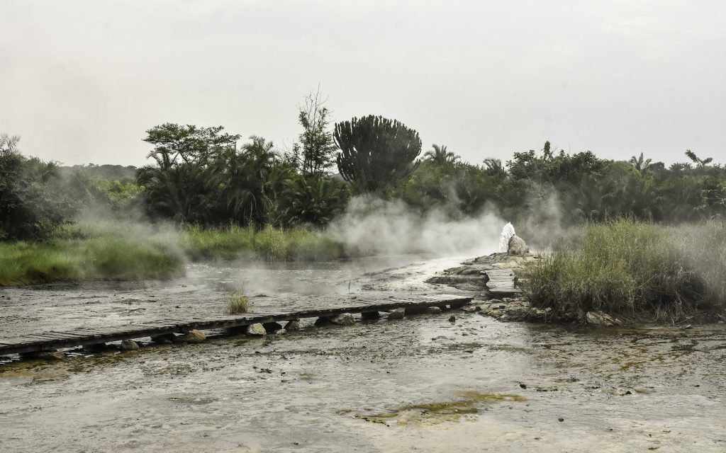 Steam drifting across the flat mineral crust of the Sempaya hot springs with forest behind