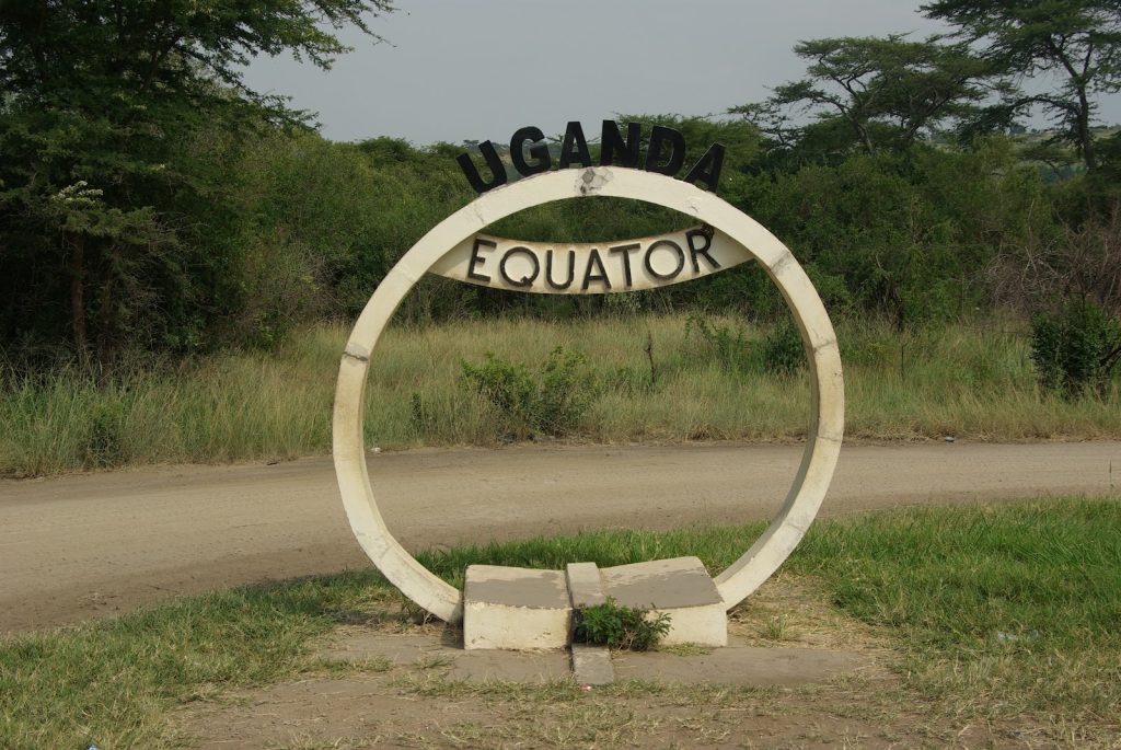 The white concrete Uganda Equator monument standing beside a dirt road in open grassland